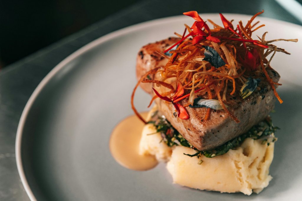 A gourmet tuna steak served on mashed potatoes with colorful garnish on a white plate.