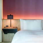 A modern, minimalist hotel room with elegant lighting and comfortable bed linen.