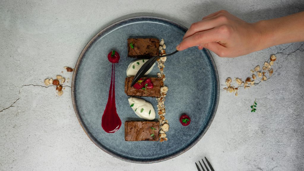 Top view of crop anonymous person holding spoon while eating delicious chocolate dessert from ceramic plate